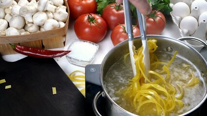 Chef cooking pasta in saucepan. Preparation italian tagliatelle in domestic kitchen. Cook with tongs mixing pasta in saucepan. Mushrooms, eggs, tomatoes, salt, parsley, chili peppers. Close-up. - Powered by Adobe