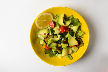 Vegetable salad made of fresh cucumbers, cherry tomatoes, avocado, lettuce salad and lemon.