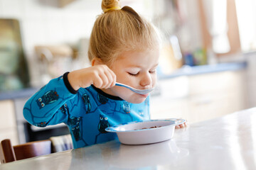 Gorgeous little toddler girl eating healthy cereal with milk for breakfast. Cute happy baby child...