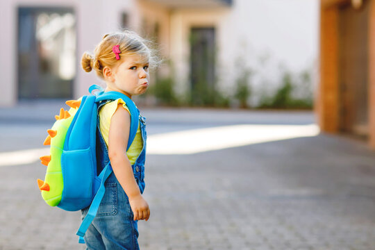 Cute Little Adorable Toddler Girl On Her First Day Going To Playschool. Healthy Upset Sad Baby Walking To Nursery School. Fear Of Kindergarten. Unhappy Child With Backpack On The City Street, Outdoors