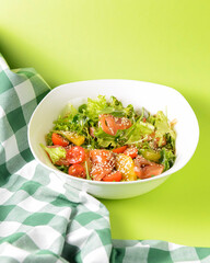 Fresh salad with salmon and vegetables close up in a bowl over bright green background with tablecloth.