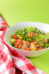 Fresh salad with salmon and vegetables close up in a bowl over bright green background with tablecloth.