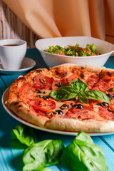 Fresh italian pizza with salami and black olives and other food on the background. Blue colored wooden table.