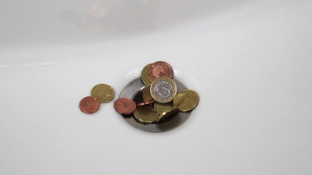 Water leaks into the sink drain over a pile of euro cents in slow motion. Coins close-up. Money laundering concept. Household expenses idea