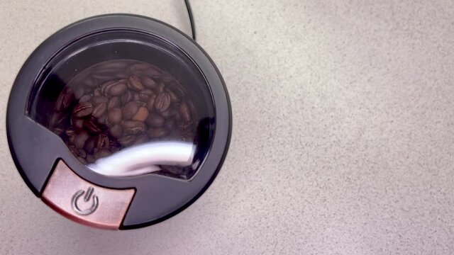 Freshly roasted coffee beans are poured into a coffee grinder. Barista prepares coffee for grinding close-up. Top view with space for text. Slow motion.