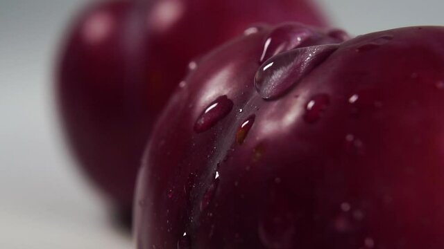 A drop of pure water drips and splashes onto the textured rind of a ripe red plum. Slow motion. Macro shot. Healthy fruit