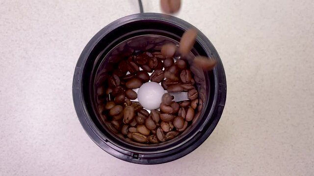 Freshly roasted coffee beans are poured into a coffee grinder. Barista prepares coffee for grinding close-up. Top view with space for text. Slow motion.
