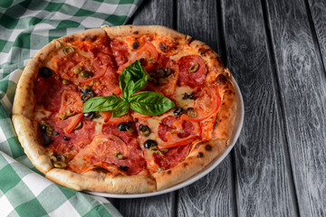 Fresh italian pizza with salami and black olives served over rustic wooden background. Traditional Italian pizza recipe