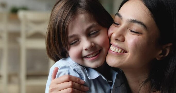 Close up cheery young Asian mother strong cuddle little Caucasian son, multi ethnic diverse family touch cheeks feeling love and devotion. Adopted 6s child and new happy mommy, caress and bond concept