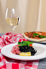 Squid Ink Black Pasta with seafood served on a white plate with a glass of white wine.