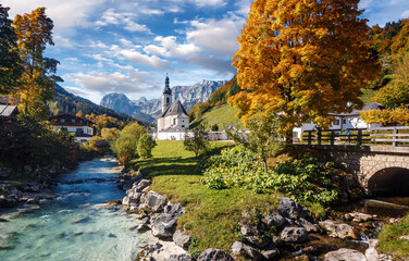 Fototapeta premium Beautiful nature landscape. Incredible autumn scenery. View on Alpine highlands with rock mountains, colorful trees and Small church on the river bank.view on famous Parish Church of St. Sebastian