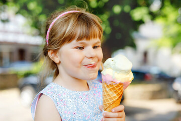 Little preschool girl eating ice cream in waffle cone on sunny summer day. Happy toddler child eat...