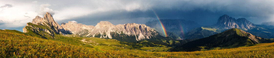 Panoramic view of idyllic mountain scenery in the Dolomites Alps with Majestic Peaks, Overcast sky and Rainbow. Odle mountain range, Seceda and Furchetta peak. Val Gardena in Dolomites. Italy.