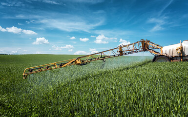 Agricultural sprayer detail. Rural landscape. Spring sunny landscape with wheat field and blue sky. Chemical fertilizers, toxic pesticides, insecticides. Ecology concept. Rich harvest concept