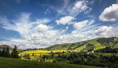 Fototapeta premium Stunning nature landscape. Amazing Sunny scenery . View on small mountain village on a rolling hills and perfect blue sky at summer day. Carpathian mountains. Ukraine