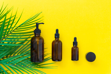 Glass bottles for cosmetics with a palm branch on a yellow background. Blank packaging without label for mockup. Natural organic cosmetics concept.