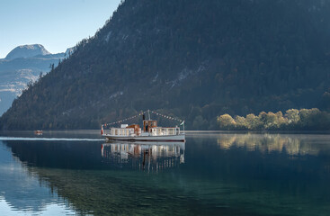 Obraz premium Amazing autumn scenery of mountain lake at sunny day. Pleasure boat on a Grundlsee lake. Austria. Amazing nature landscape. Picture of alps calm lake. concept of an ideal resting place