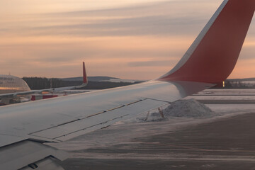 Fototapeta na wymiar Yekaterinburg. Russia. 12/20/2020. The view from the airplane window of the runway and part of the silvery-red wing during takeoff at dawn. Ural Airlines. Aeroflot