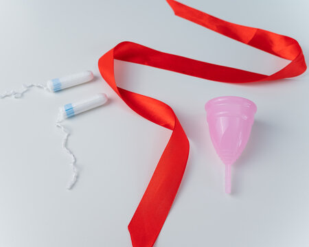 Tampon, pink menstrual cup and red satin ribbon on a white background. Means of intimate hygiene of a woman during mentruation