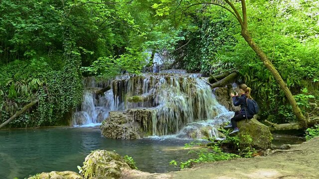 Video with a girl taking pictures and enjoys a beautiful waterfall in green spring forest, Krushuna falls, Balkan Mountains, Bulgaria..