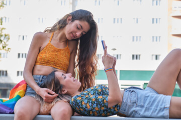 Lesbian couple sitting and laying at street checking the smartphone.
