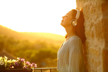 Woman resting in a balcony listening to music with headphones
