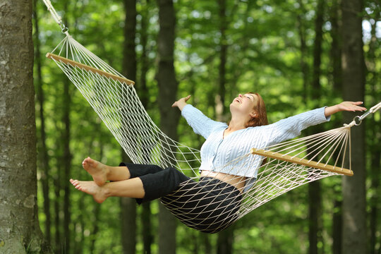 Happy woman swinging on hammock in a forest - Powered by Adobe