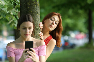 Woman using phone being spied by her friend