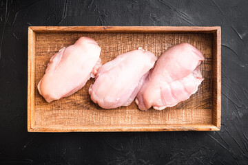 Fresh chicken meat, in wooden box, on black stone background, top view flat lay
