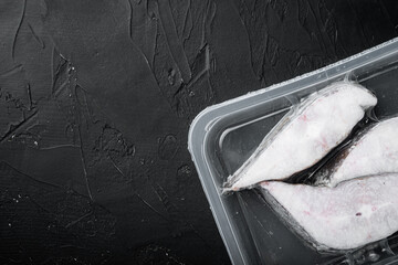 Frozen Greenland halibut steaks vacuum pack, on black dark stone table background, top view flat...