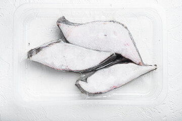 Frozen Greenland halibut steaks vacuum pack, on white stone table background, top view flat lay