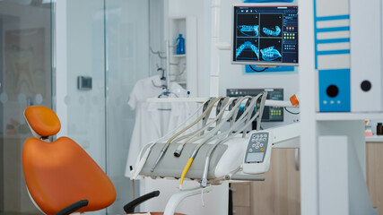 Close up revealing shot of medical orthodontist monitor with teeth x ray images on it. Empty modern clinic stomatology chair with nobody in it. Professional dentistry equipment with dental tools
