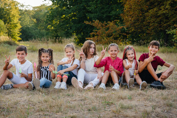 Fototapeta premium A large group of cheerful children sit on the grass in the Park and smile. Games in a children's camp
