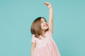 Little fun kid girl 5-6 years old wears pink dress hold hand above head show how much she grown try...
