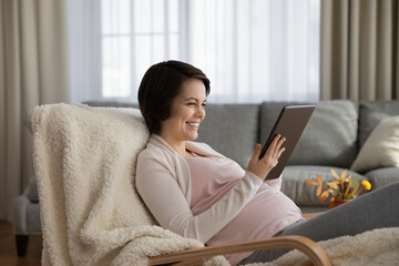 Happy pregnant woman using tablet, having fun with device at home, smiling young future mom typing and looking at screen, chatting in social networks or shopping online, pregnancy and motherhood