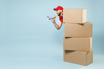 Full size body length fun delivery guy employee man in red cap white T-shirt vest uniform work dealer courier hold blank cardboard box isolated on pastel blue color background studio. Service concept.