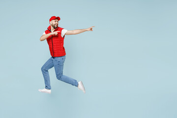 Fototapeta na wymiar Full size body length side view delivery guy employee man in red cap white T-shirt vest uniform work dealer courier jump run go walk isolated on pastel blue color background studio. Service concept