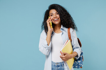 Young smiling african american girl teen student in denim clothes backpack hold books use mobile...