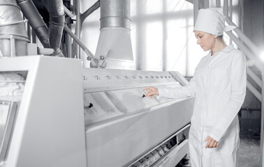 Fototapeta na wymiar Woman operator checks quality of finished food products wheat flour. Modern electrical mill machinery for production