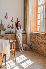 serious young asian woman in earphones standing with crossed hands in kitchen