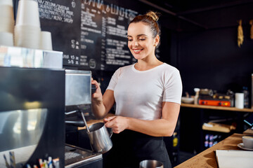 Fototapeta na wymiar Female barista preparing milk for cappuccino in coffee shop