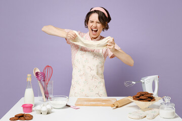 Young sad stressed nervous housewife cook chef baker woman war pink apron work at table kitchenware kneads dough baking scream isolated on violet background studio Process cooking food pastry concept.