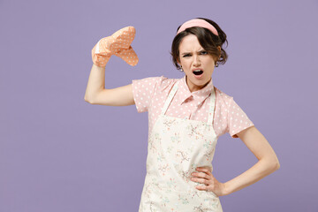Young angry indignant displeased dissatisfied housewife housekeeper chef cook baker woman in pink apron potholder stand akimbo arm on waist isolated on pastel violet background. Cooking food concept.