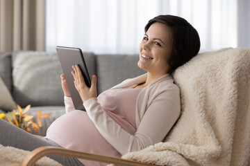 Smiling dreamy pregnant woman using tablet, dreaming about good future, having fun with device, young attractive female chatting in social networks or shopping online, pregnancy and motherhood