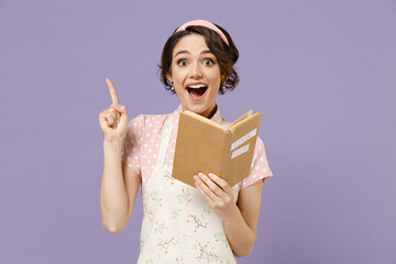 Young insighted proactive housewife housekeeper chef cook baker woman wearing pink apron read cook book point finger with idea of new recipe isolated on pastel violet background Cooking food concept