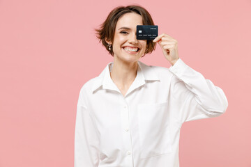 Cheerful young employee business secretary woman 20s corporate lawyer in classic formal white shirt work in office cover eye with credit bank card isolated on pastel pink background studio portrait.