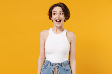 Young surprised amazed surprised shocked caucasian woman 20s with bob haircut wearing white tank top shirt looking aside isolated on yellow color background studio portrait. People lifestyle concept