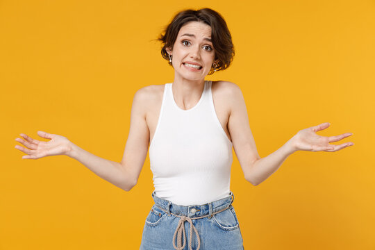 Young confused uncertain doubtful sad woman 20s with bob haircut wearing white tank top shirt spread hands look camera oops gesture isolated on yellow color background studio People lifestyle concept