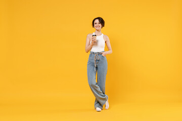 Fototapeta na wymiar Full length young fun happy smiling woman 20s with bob haircut wear white tank top shirt hold takeaway delivery craft paper brown cup coffee to go isolated on yellow color background studio portrait.