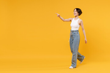 Fototapeta na wymiar Full length side view young woman 20s with bob haircut wear white tank top shirt walking go point index finger aside on workspace area mock up isolated on yellow background People lifestyle concept